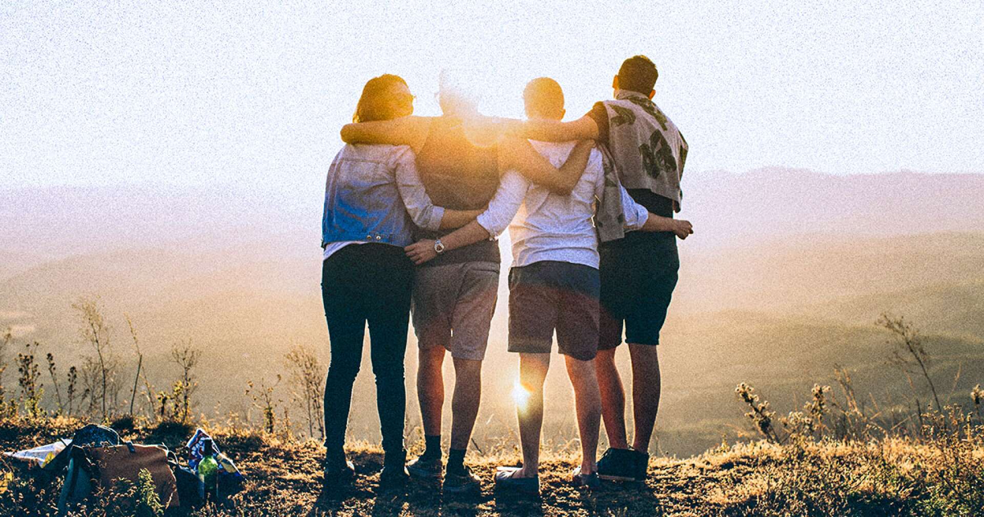 Vier Freunde stehen Arm in Arm und betrachten den Sonnenuntergang