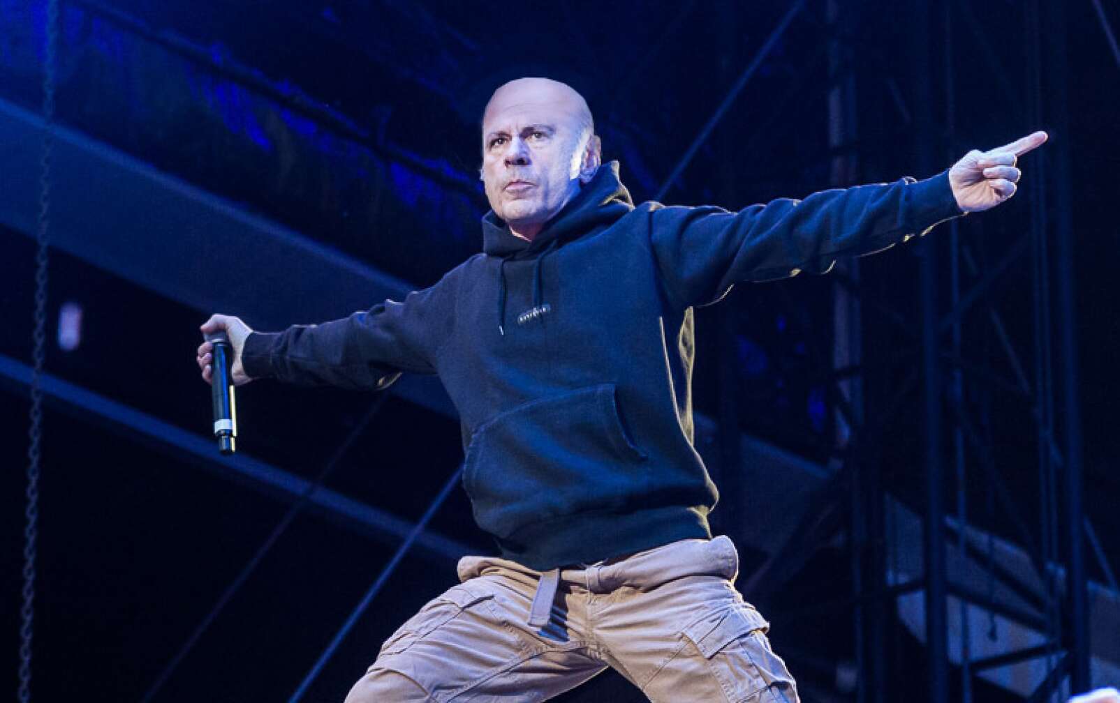 Bruce Dickinson steht in der Hocke, mit Hoodie und Cargohose auf der Bühne