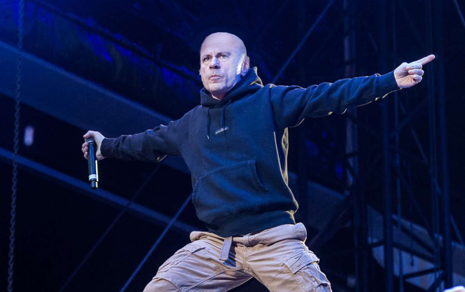 Bruce Dickinson steht in der Hocke, mit Hoodie und Cargohose auf der Bühne
