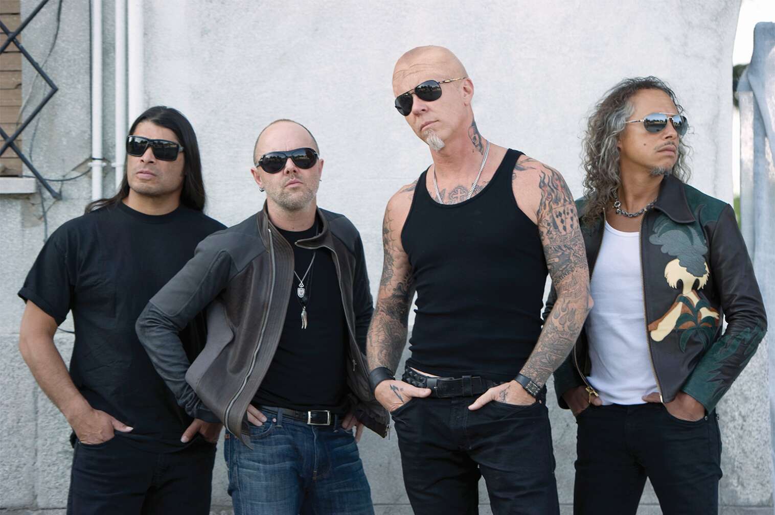 Metallica posieren nebeneinander vor einer weißen Hauswand