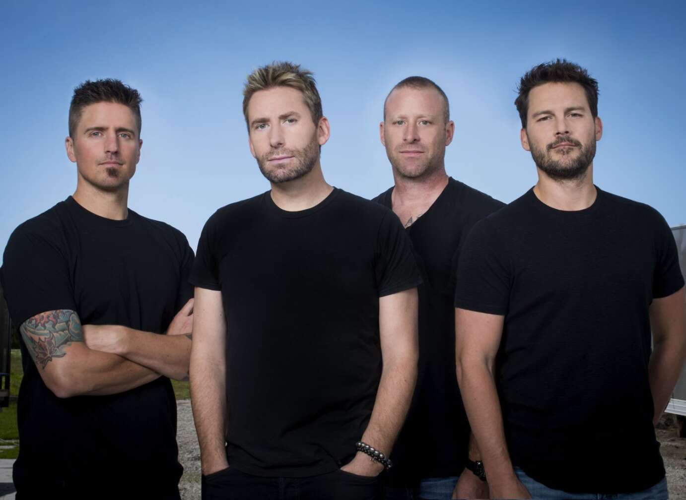 Nickelback stehen in schwarzen T-Shirts vor himmelblauem Hintergrund