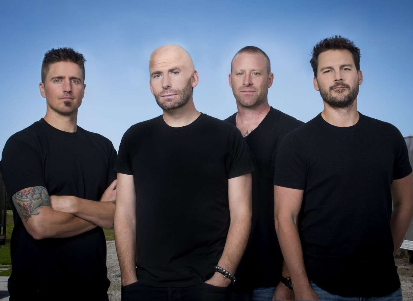 Nickelback stehen in schwarzen T-Shirts vor himmelblauem Hintergrund