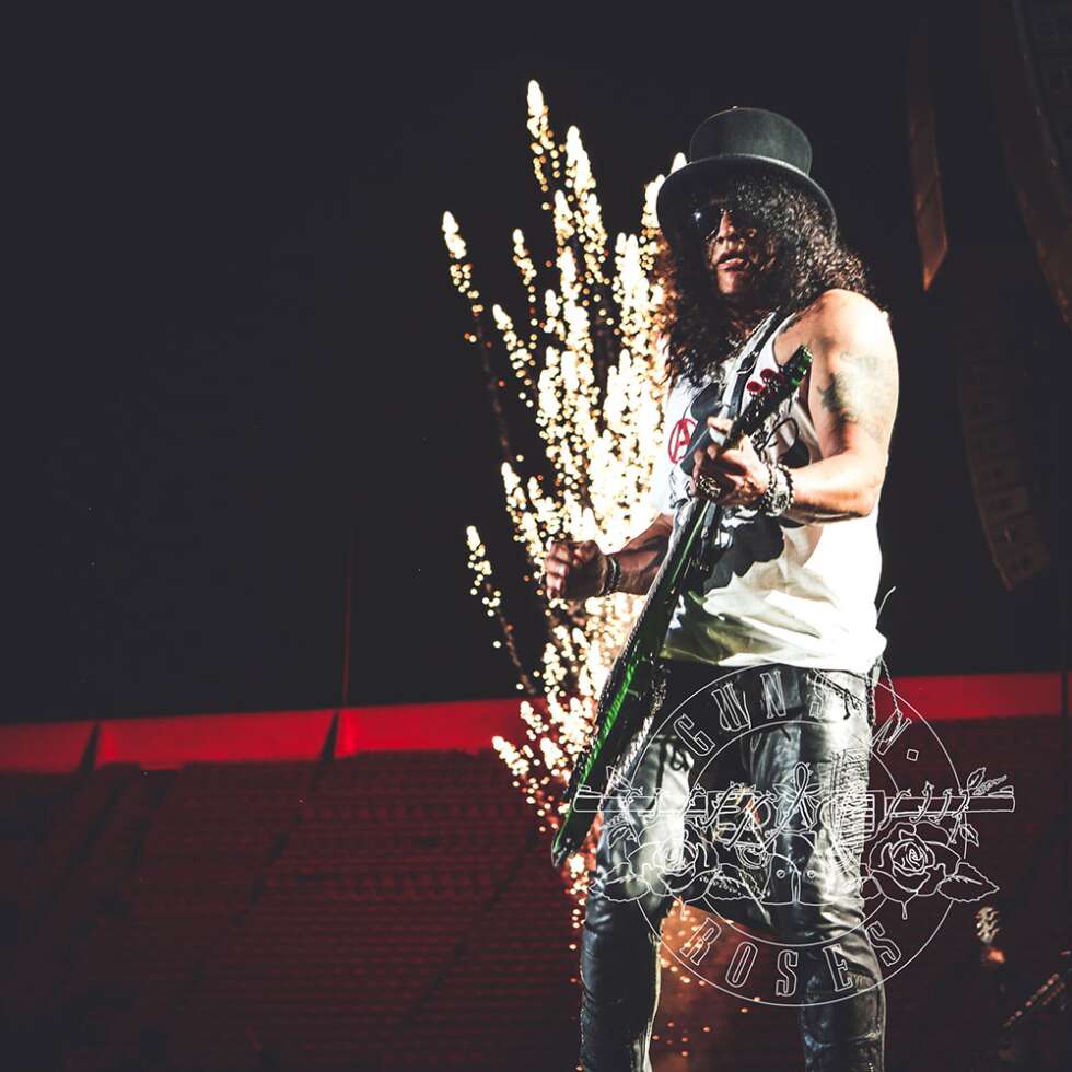 Slash zockt auf seiner Gitarre mit Bühnenfeuerwerk im Hintergrund