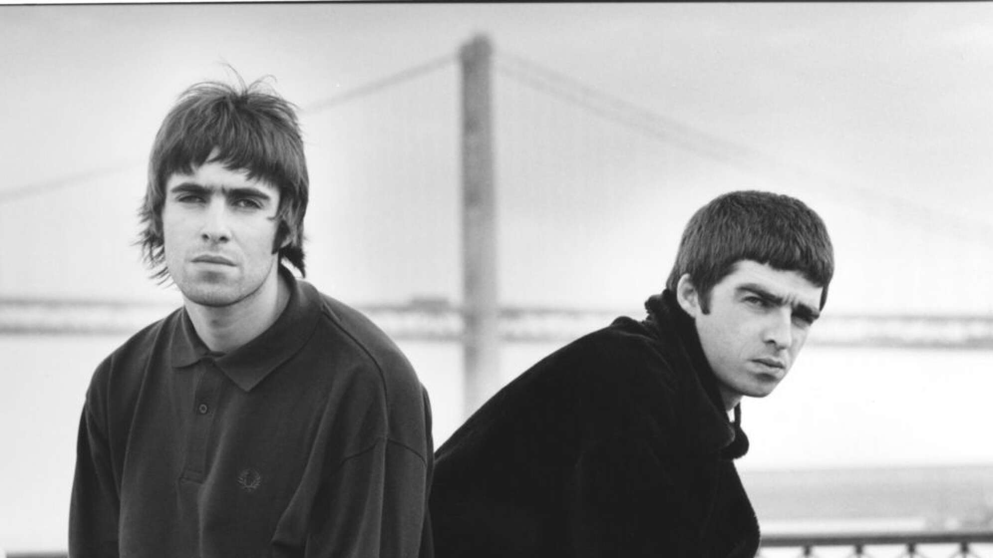 Noel und Liam Gallagher sitzend auf Bank, mit ernstem Blick