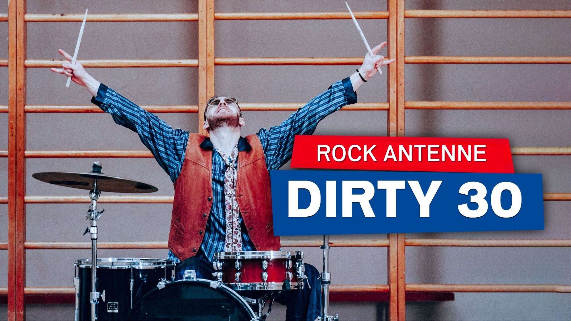 Ein Schlagzeuger sitzt in einer Turnhalle am Schlagzeug, reckt beide Hände mit Drumsticks im Jubel in die Luft - dazu der Text: ROCK ANTENNE Dirty 30