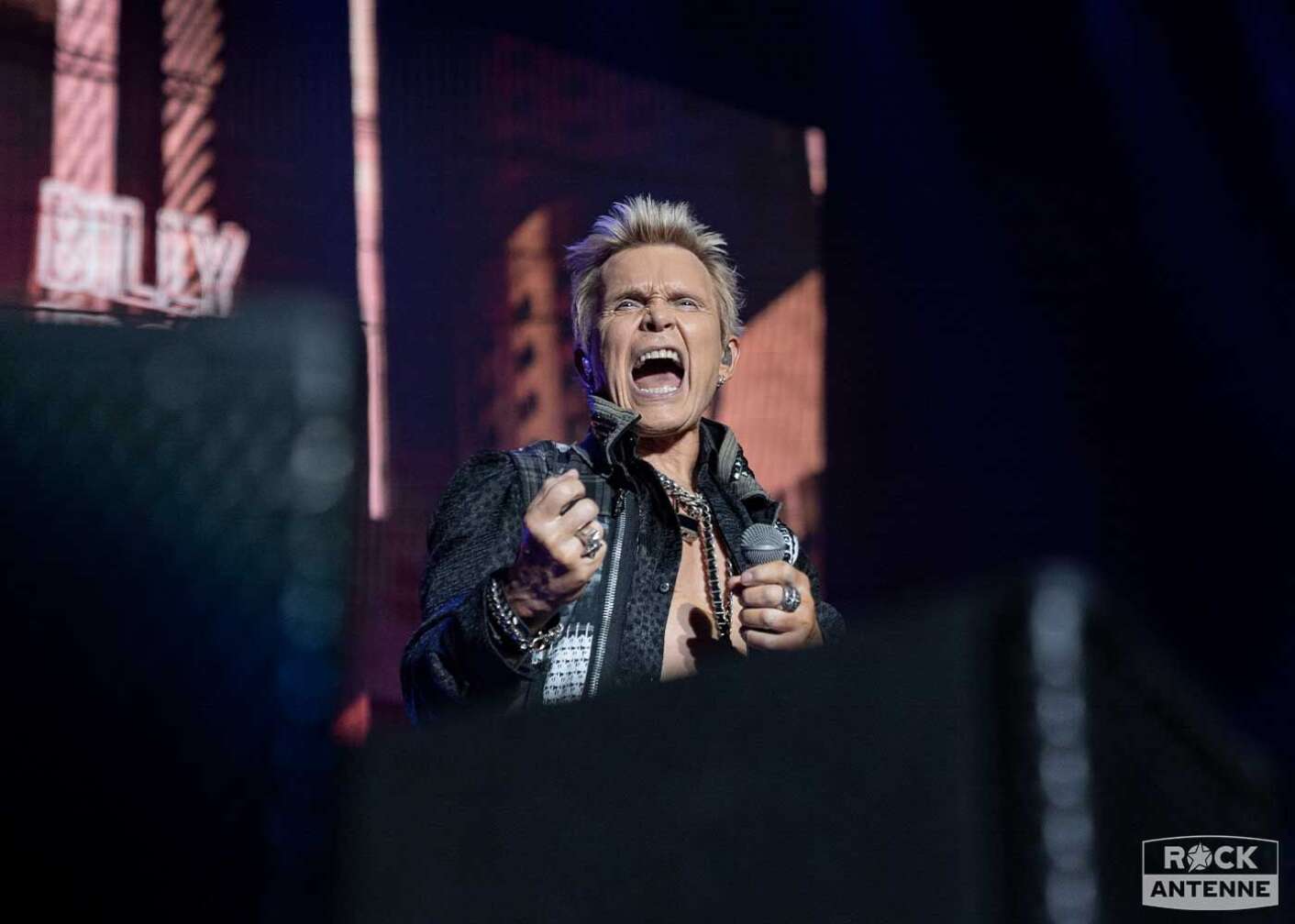 Billy Idol schreit mit aufgerissenem Mund auf der Bühne