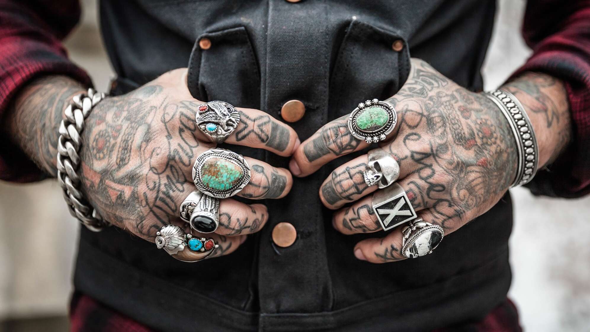 Hände mit Tattoos und Ringen, in Westentasche liegend