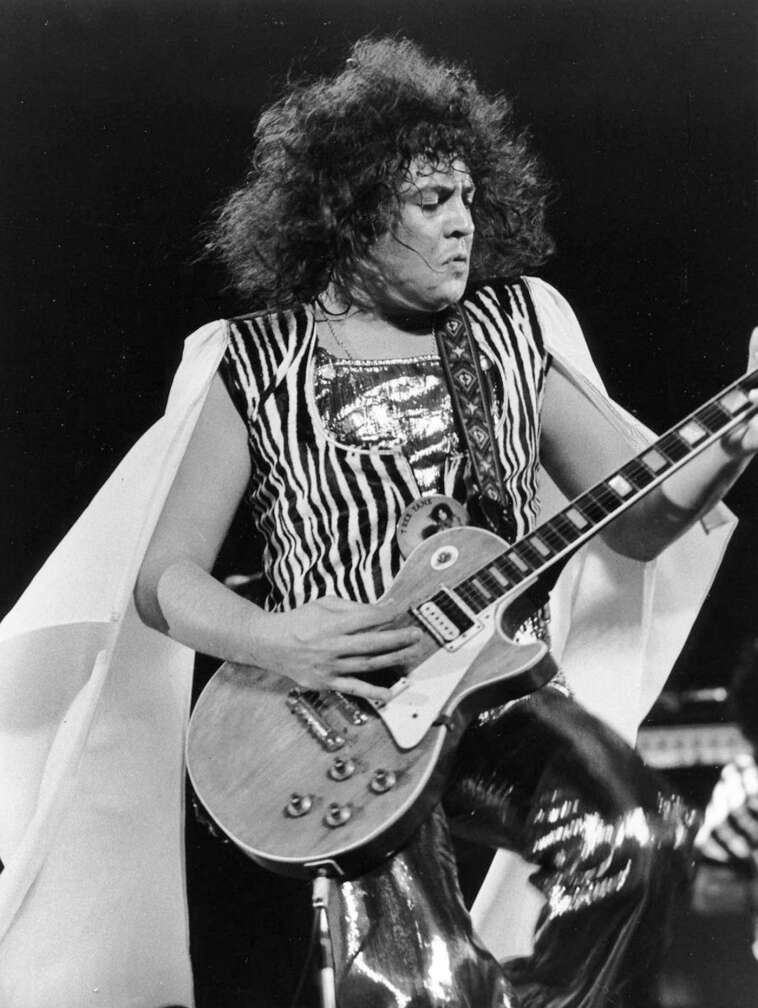 Marc Bolan steht mit Gitarre und Cape auf der Bühne