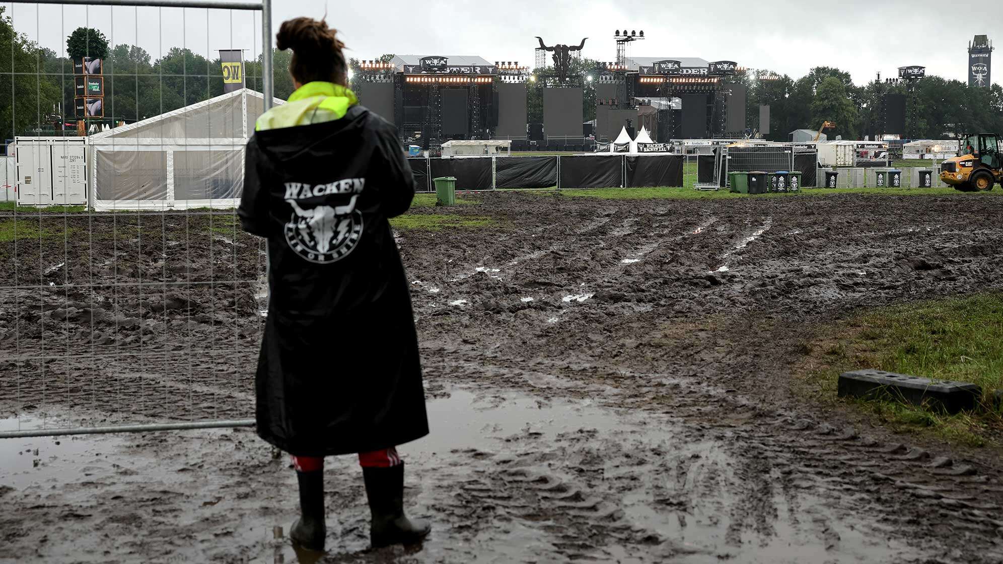 Ein Metal-Fan steht vor einem noch geschlossenen Einlass zu den beiden Hauptbühnen auf dem vom Regen aufgeweichten und schlammigen Festivalgelände.