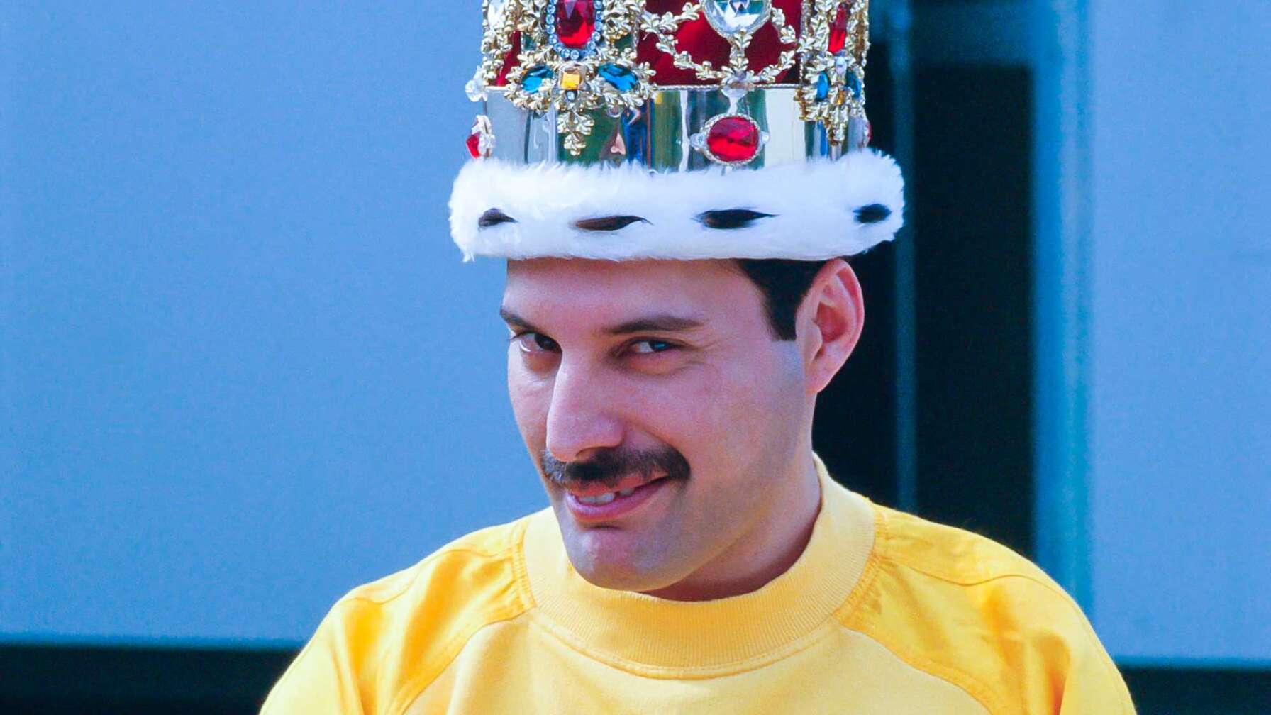 Ein Pressefoto von Freddie Mercury - der Sänger trägt eine Krone auf dem Kopf und lächelt in die Kamera.