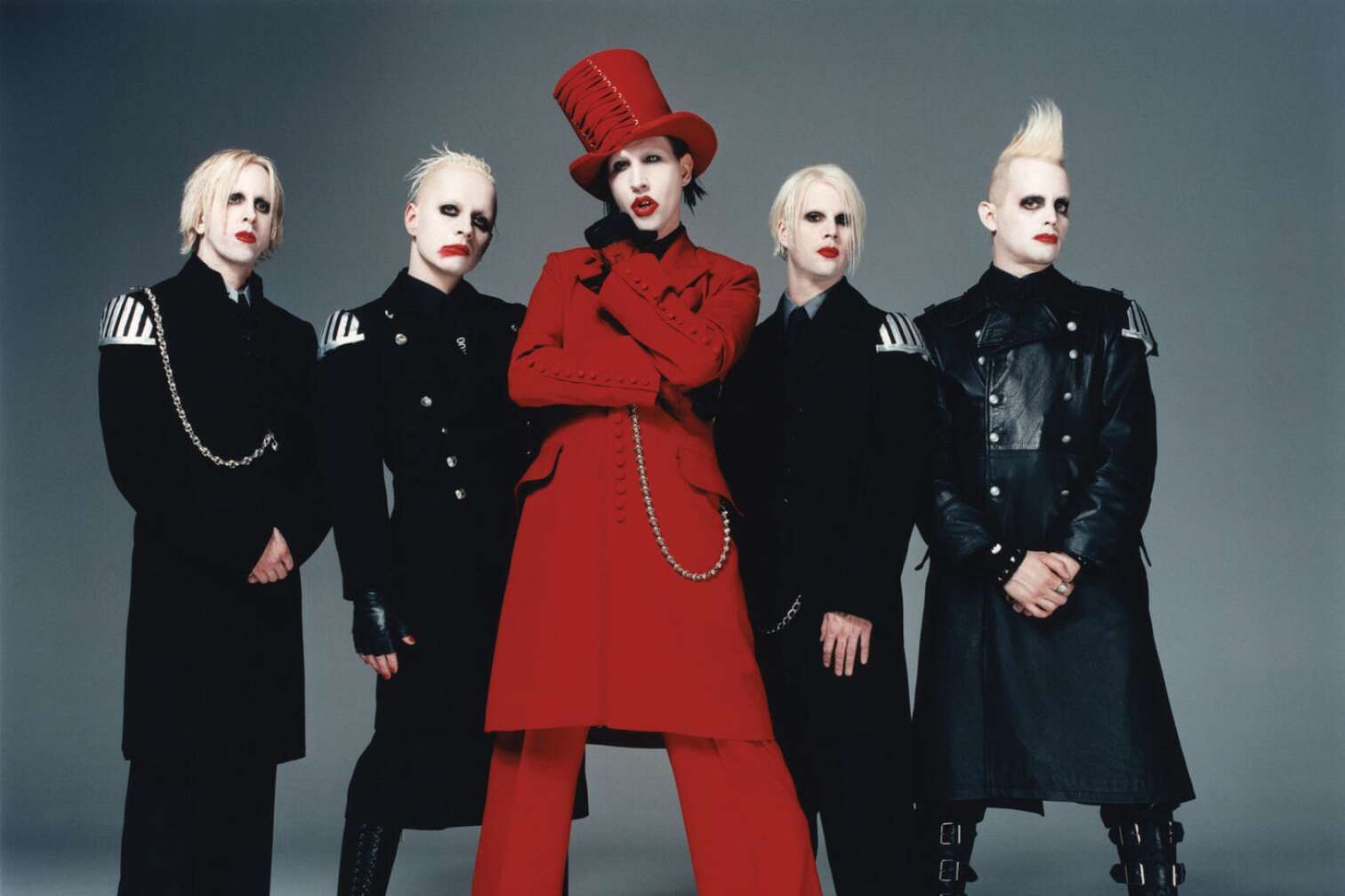 Marilyn Manson in einem roten Mantel und Hut umgeben von seiner Band
