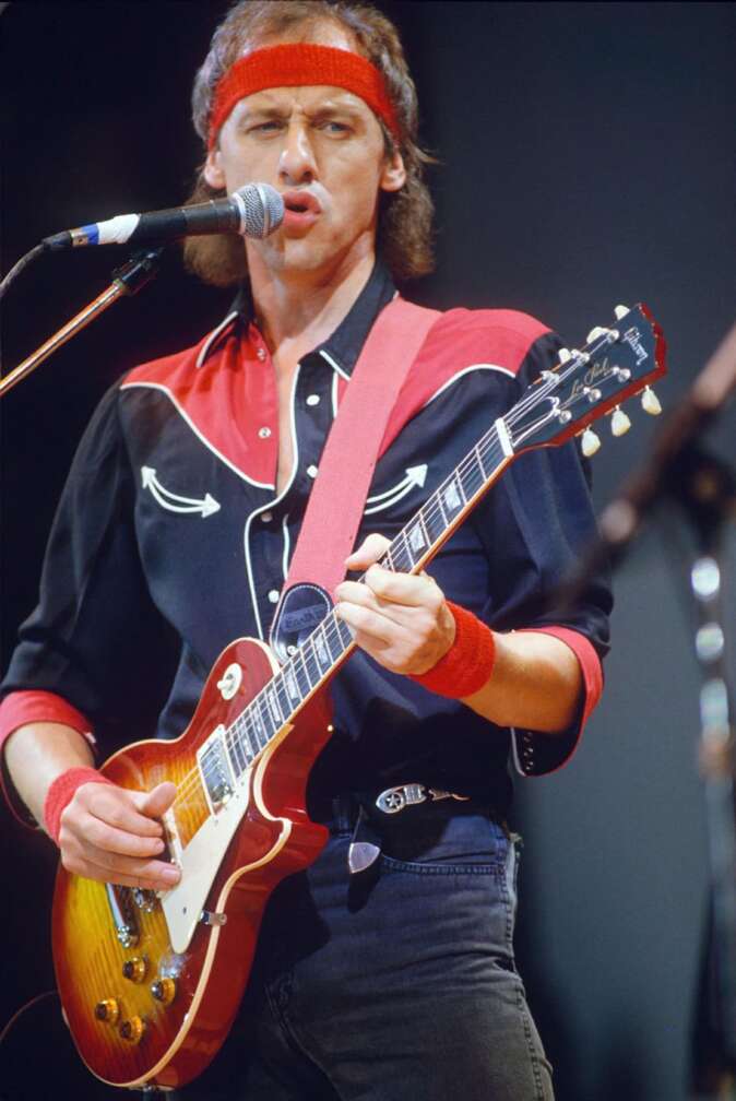 Mark Knopfler mit einem roten Stirnband spielt Gitarre