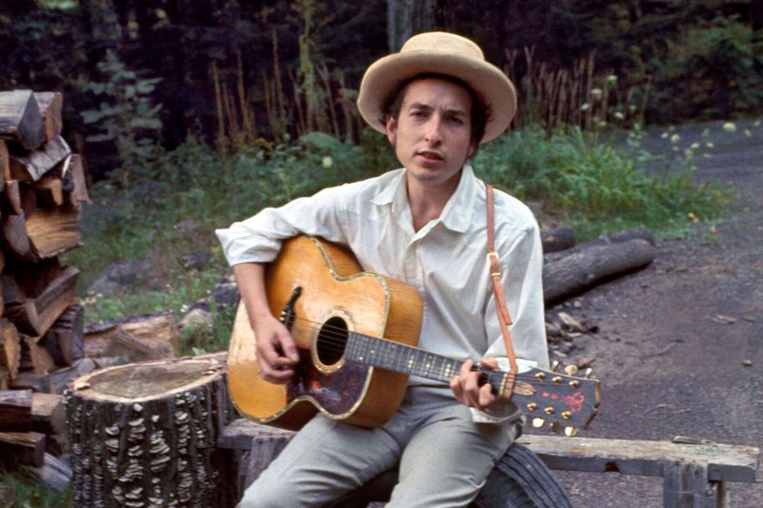 Bob Dylan sitzt auf Band im Wald und spielt Gitarre