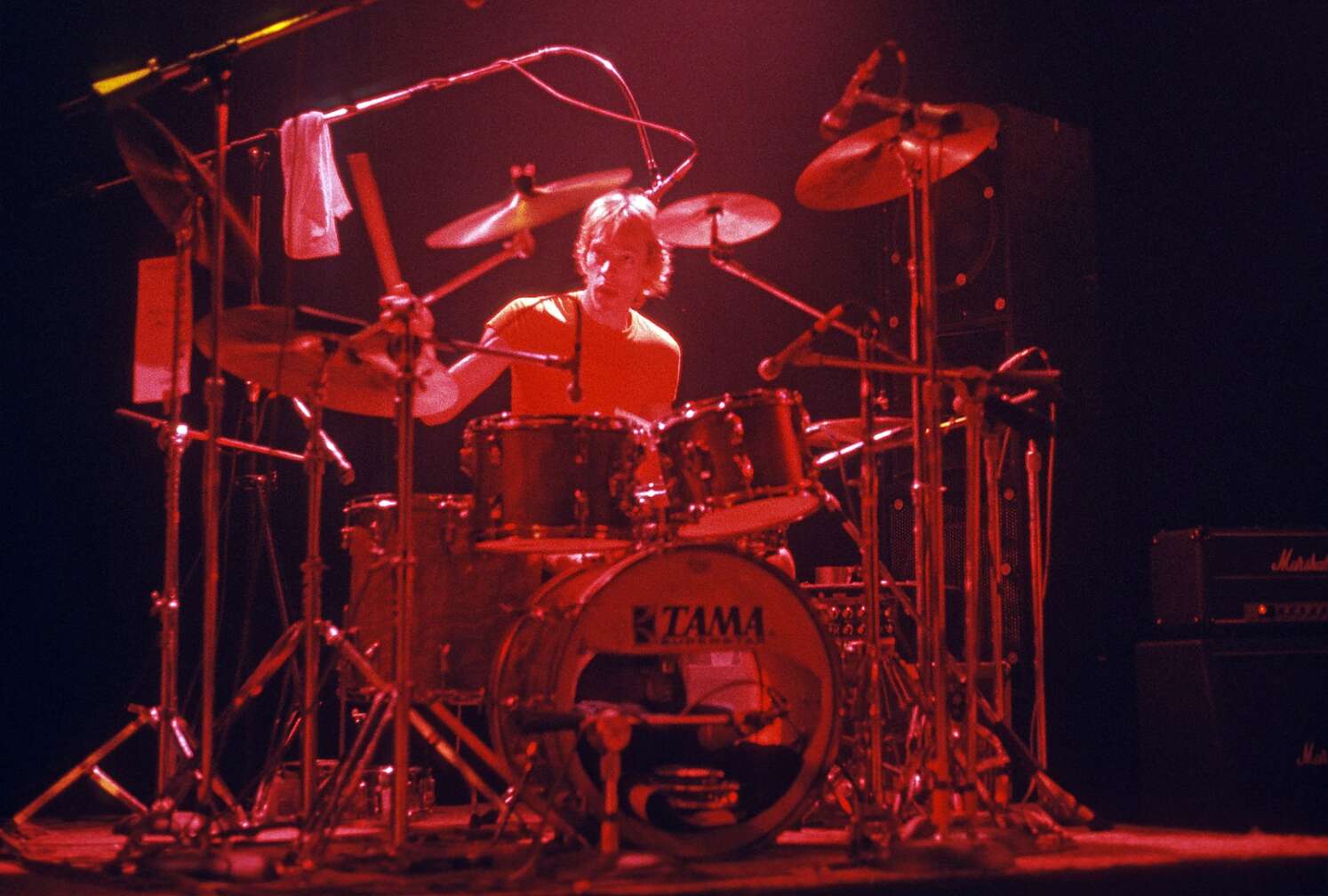 Stewart Copeland im roten Scheinwerferlicht hinter seinem Schlagzeug