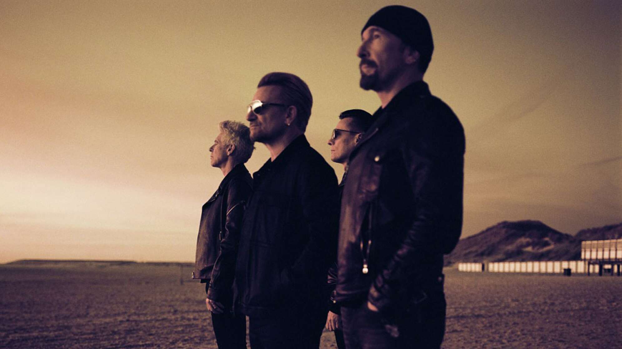 Die Mitglieder von U2 stehen an einem Strand und blicken in die Ferne