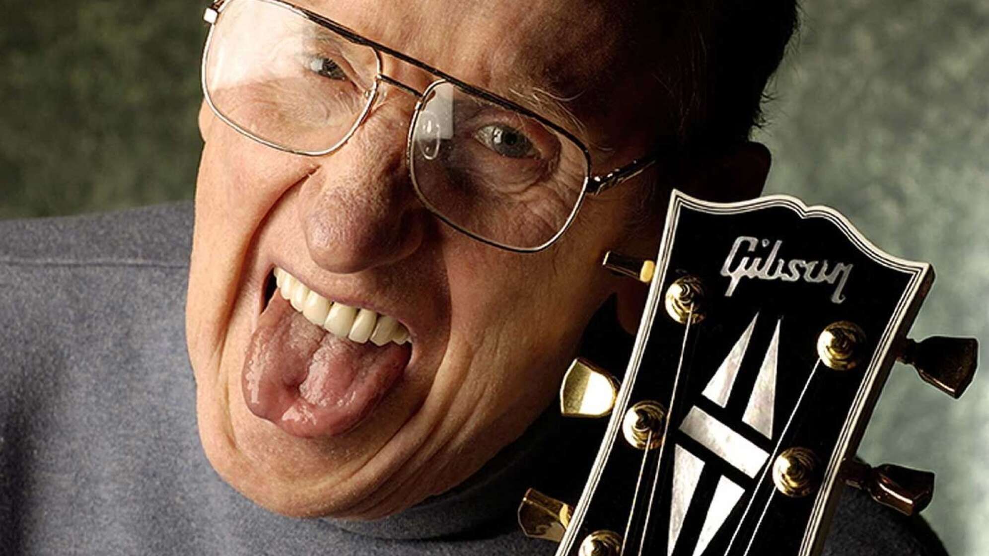 Les Paul-Gründer mit rausgestreckter Zunge und einer Gitarre